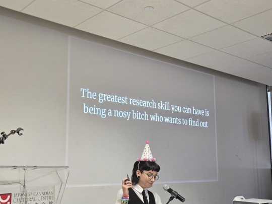 photo from dashcon2. girl with party hat in front of projected slide show that says: "the greatest research skill you can have is to be a nosy bitch who wants to find out"